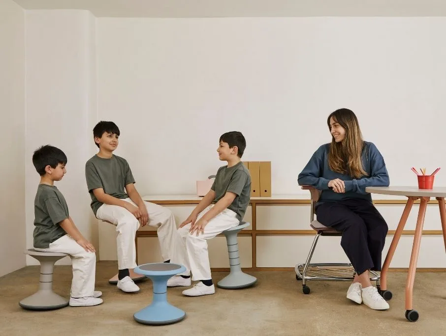 three students sitting on a classroom with their teacher watching